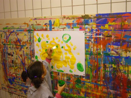EIn Kind malt mit dem Pinsel gelbe und grüne Farbe auf ein großes Papier.