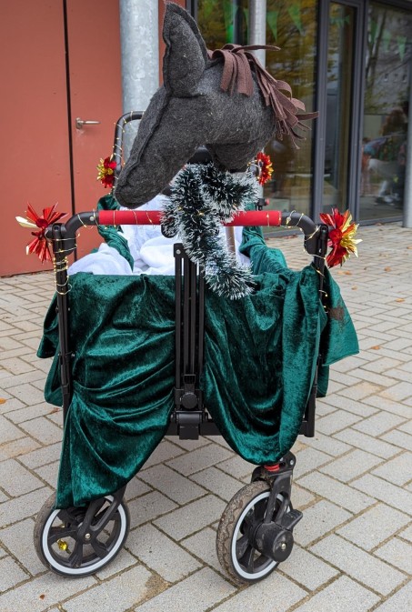 Ein Kinderwagen verhüllt in grünem Stoff mit einem Stockpferd vorne dran.