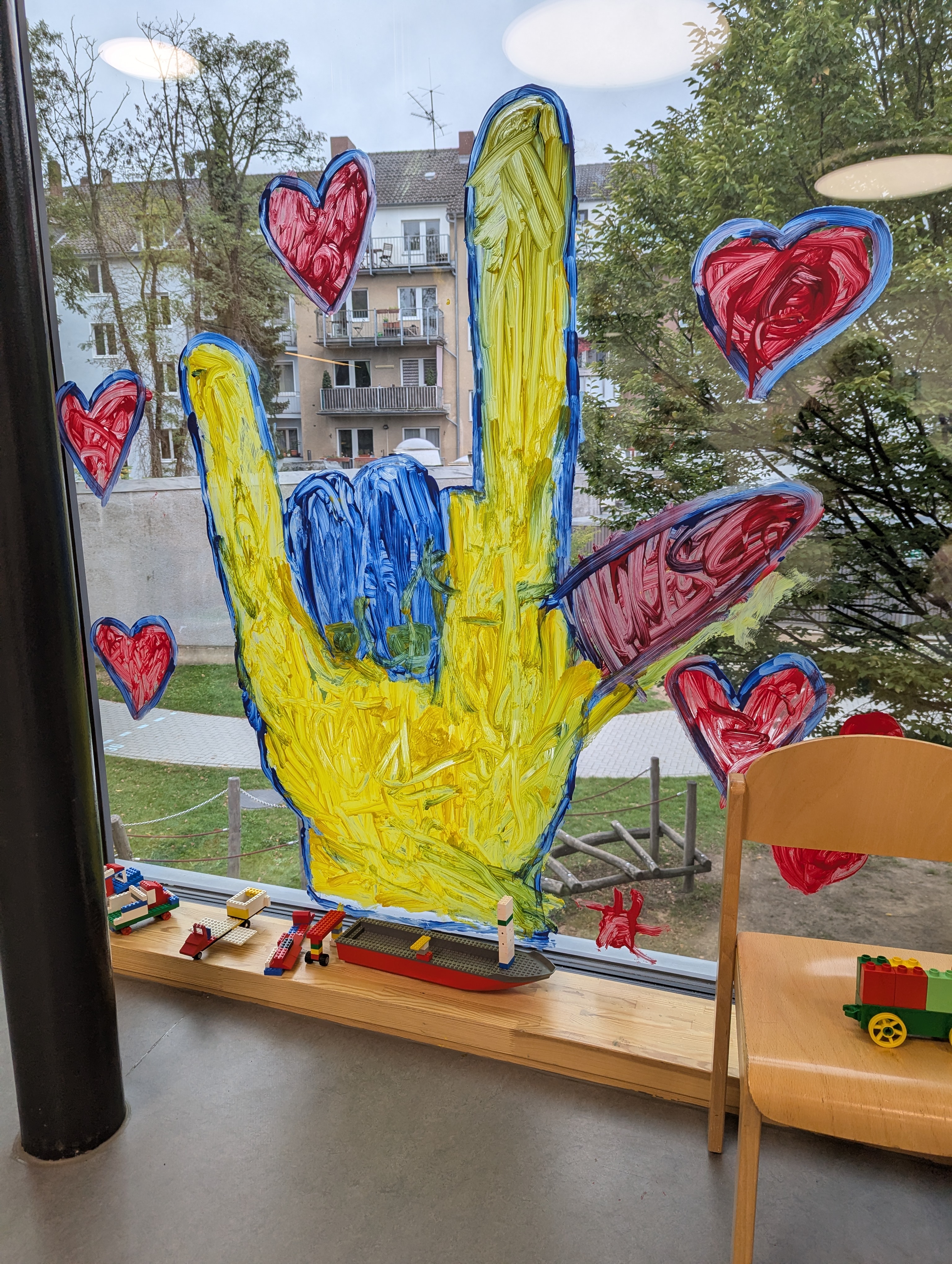 Fensterbild einer großen Hand in ILY-Form umrandet mit roten Herzen.