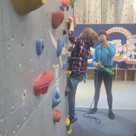 Ein Kind klettert an der Wand und wird durch einen Trainer gesichert.