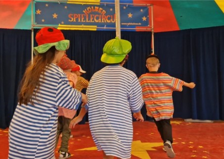 Als Clown verkleidete Kinder laufen im Kreis.