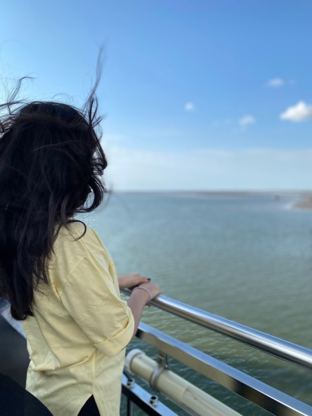 Ein Frau mit langen schwarzen Haaren blickt auf das Meer im Hintergrund.