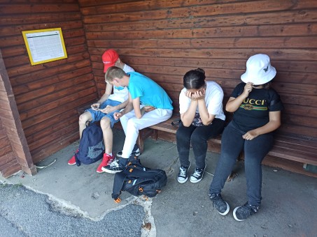 Vier Personen sitzen auf einer Bank an einer Haltestelle.