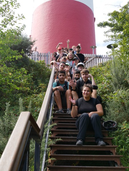 Die Jugendlichen sitzen hintereinander auf einer Treppe unterhalb des Leuchtturms.