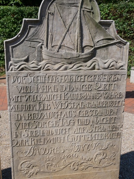 Ein alter Grabstein mit einem Schiff und viel Text.