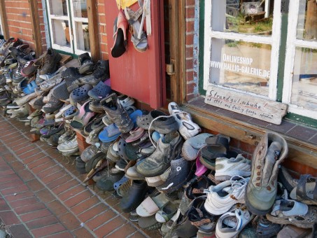 Ganz viele alte Schuhe liegen aufgereiht vor einem Haus.