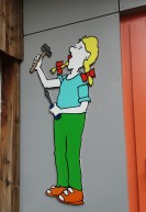 An einer Wand hängt die Figur einer Frau, die Hammer und Schraubendreher in den Händen hält.