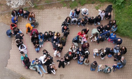 Der Schriftzug "WE" mit Personen gebildet und von oben fotografiert.
