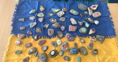 Viele bemalte Steine liegen auf einem gelb-blauen Tuch.