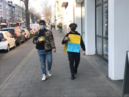 Zwei Jungen gehen mit Spendendose und Plakat auf dem Gehweg.