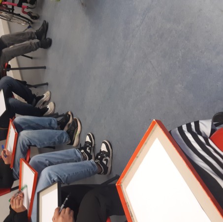 Die Beine der Kinder im Sitzkreis mit leeren, weißen Blättern auf dem Schoß.