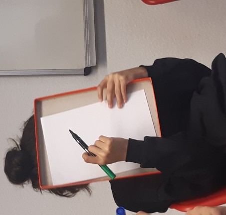 Ein Kind hält sich sich das leere, weiße Papier und einen Stift vor das Gesicht.