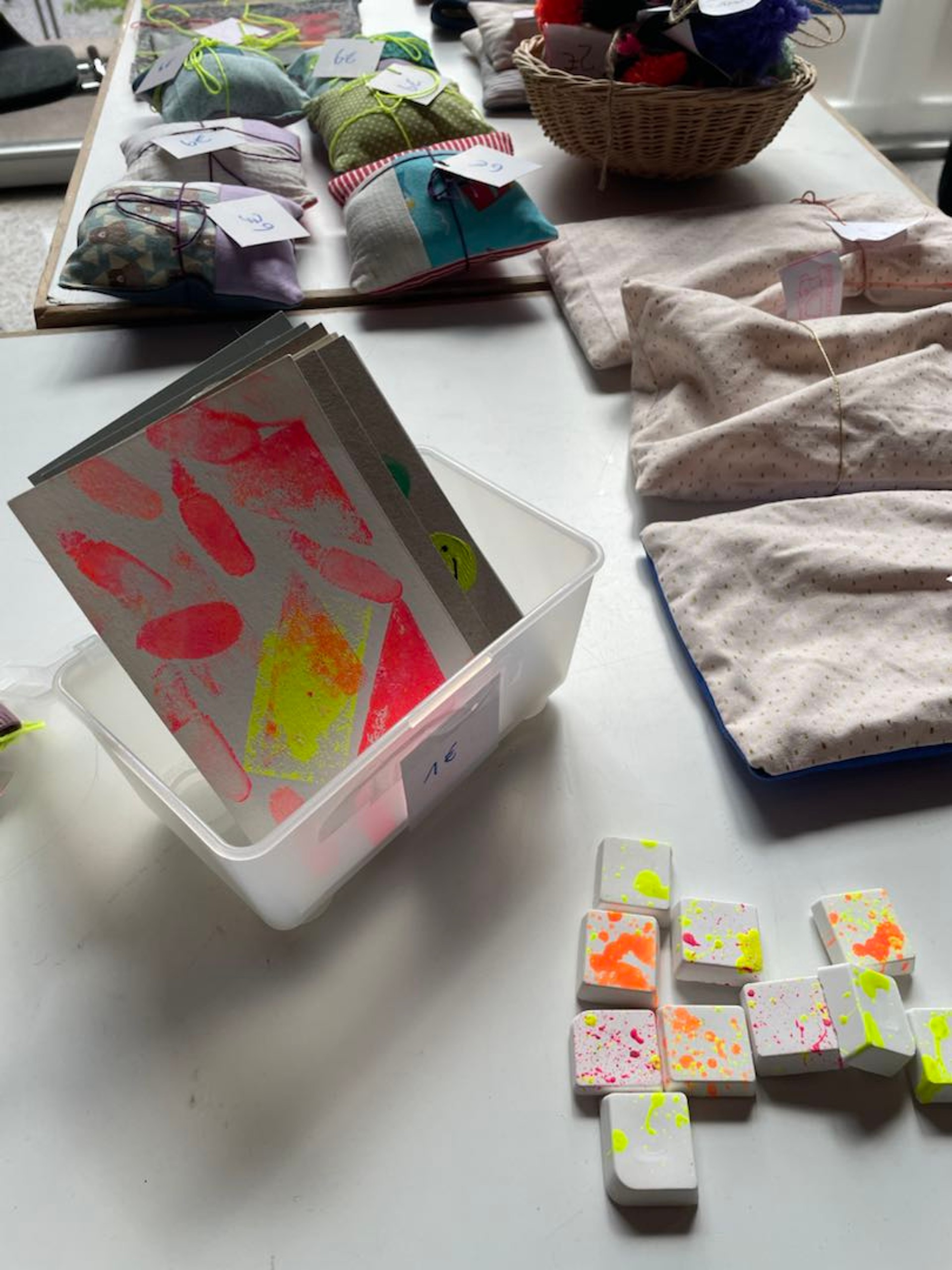 In einer Plastikbox stehen bedruckte Postkarten, daneben liegen mit bunten Farbklecksen bedruckte Magnete