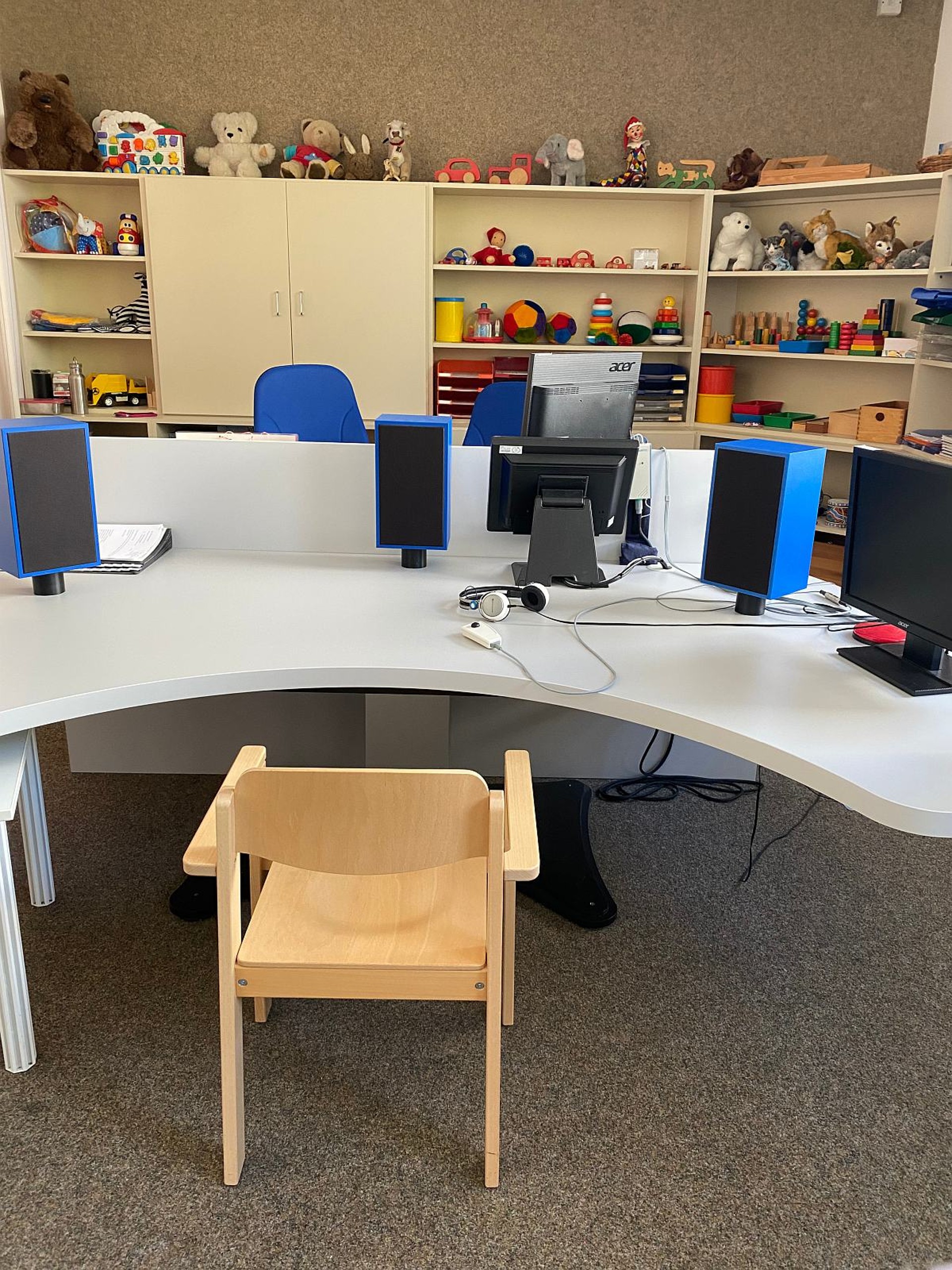 Ein Tisch mit technischen Geräten zur Hörüberprüfung. Im Hintergrund sind Regale mit bunten Utensilien zu sehen.