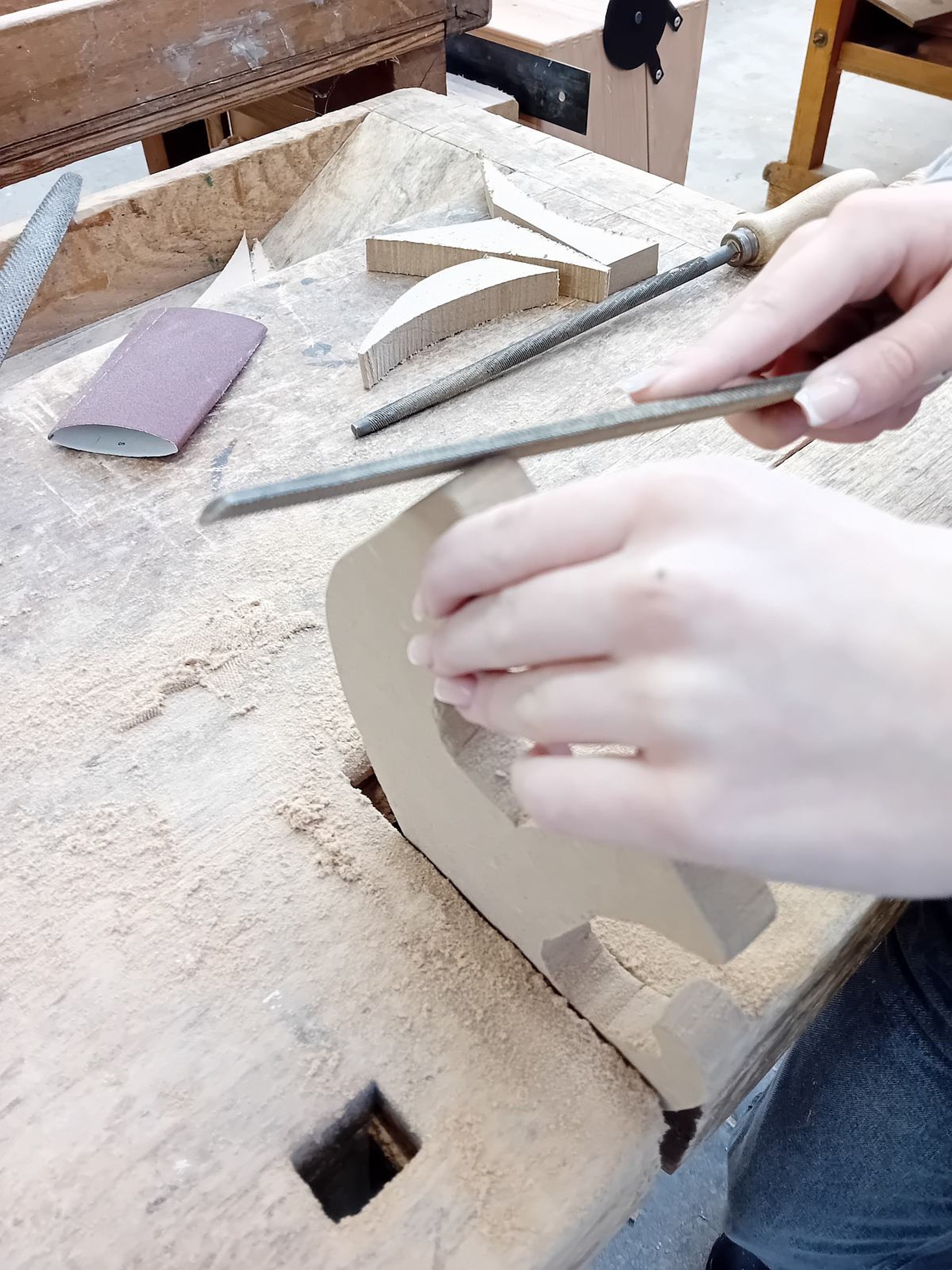 An einer Werkbank wird an einem Stück Holz gefeilt