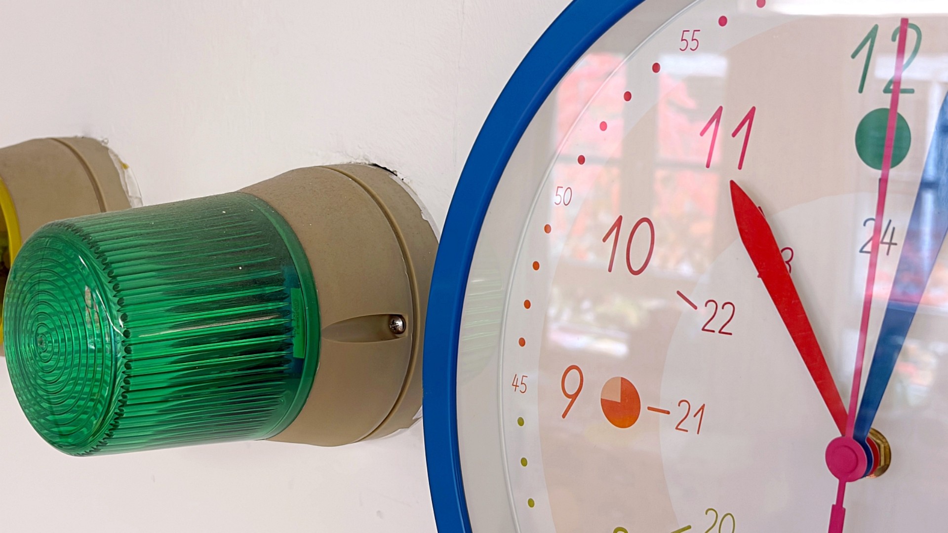 An einer Wand hängt eine große Uhr, daneben eine grüne Lampe, die ein akustisches Signal wiedergeben kann.