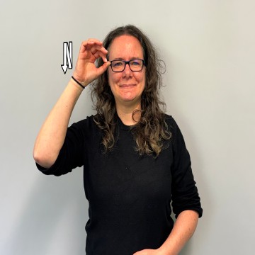 Profilfoto der Sekretärin für das Gemeinsame Lernen und die Frühförderung. Braune Locken, Brille und helle Haut. Der Gebärdenname ähnelt dem der Gebärde für "EULE".