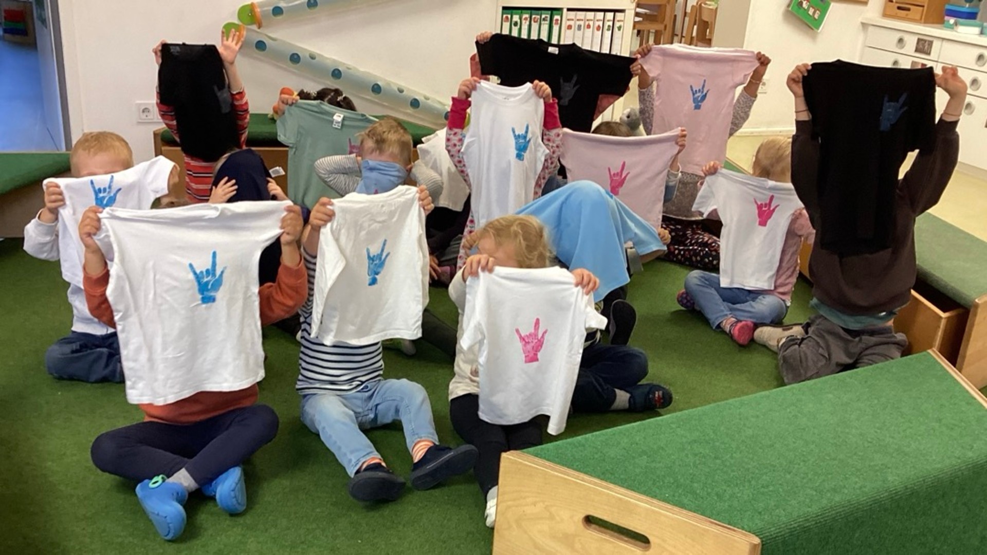 Kinder halten ihr bedruckten T-Shirts hoch.
