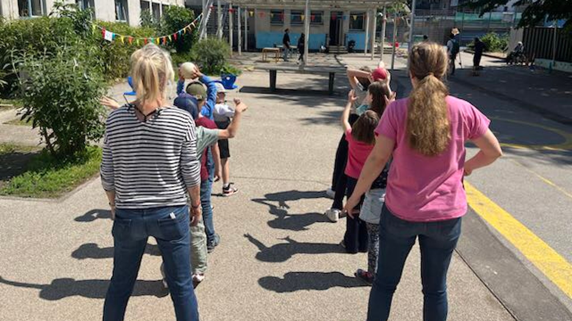 Etwa 50 sommerlich gekleidete Kinder und Eltern sitzen auf Decken, Bänken und einer Tischtennisplatte und scheun interessiert auf etwas, das nicht im Bild zu sehen ist