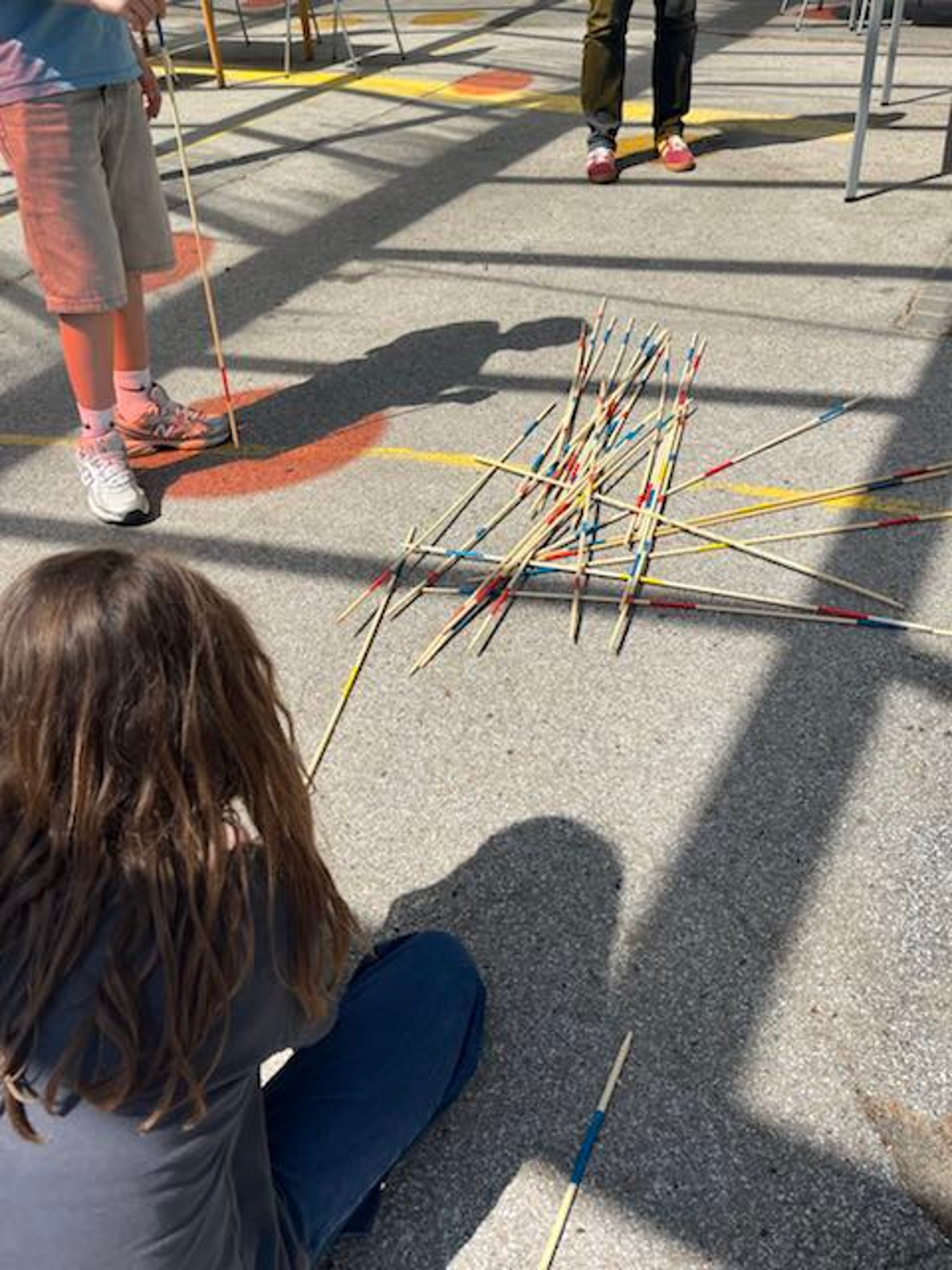 Kinder spielen das Spiel Mikado mit sehr großen Mikado-Stäben auf dem Boden.