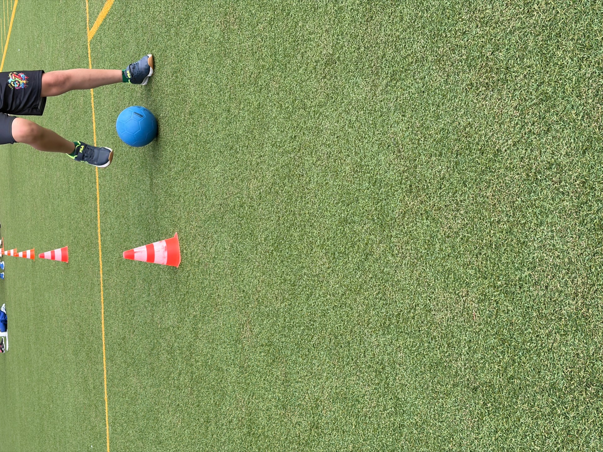 Foto von Schüler, der beim Fußball-Parcours einen Fußball im Slalom dribbelt in Bewegung. Zu sehen sind die Beine und ein blauer Ball.