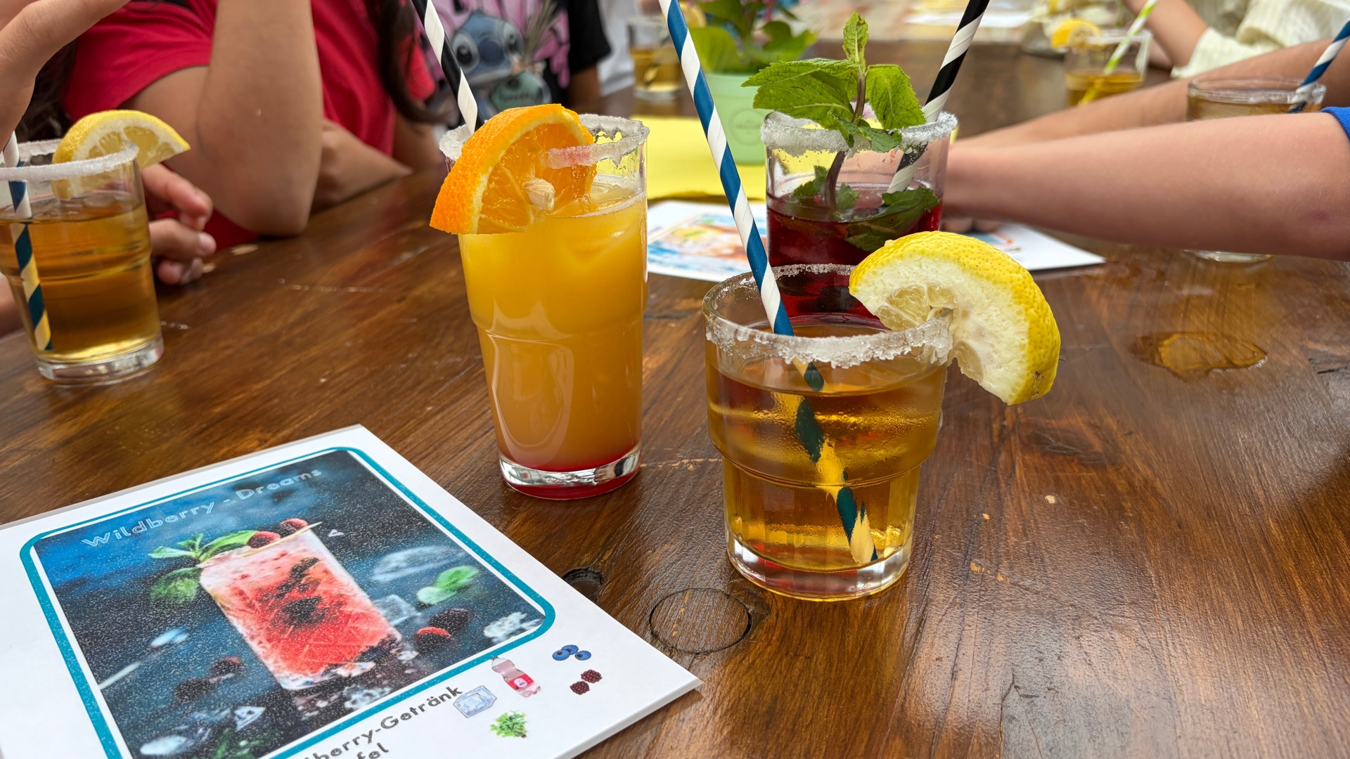 Foto der Schrägansicht auf Bierbank-Tisch. Zentral zu sehen sind die drei fertig gemixten Saft-Cocktails.