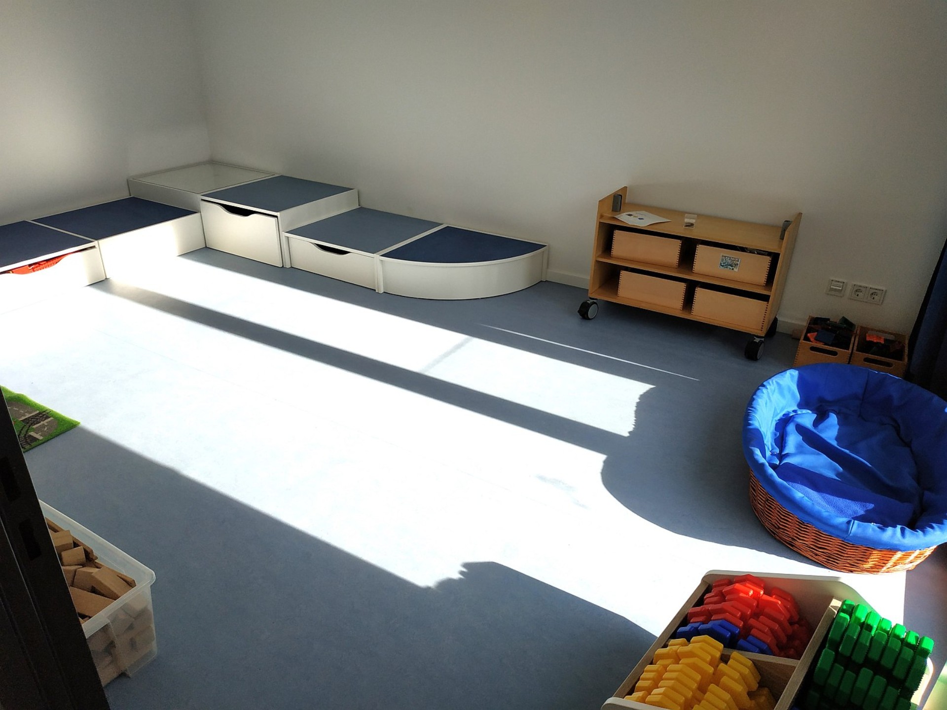 Blauer Gruppenraum mit Trittstufen und Spielmaterial wie Bausteinen.