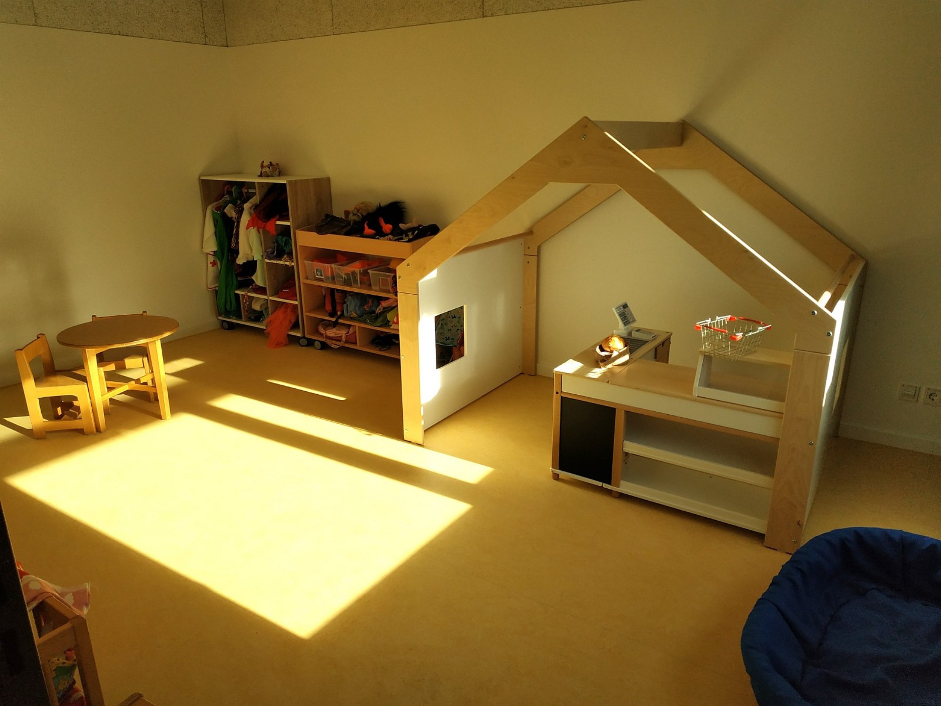 Gelber Raum mit großem Einkaufsladen-Spiele-Häuschen und Verkleidungen und Utensilien für das Rollenspiel.