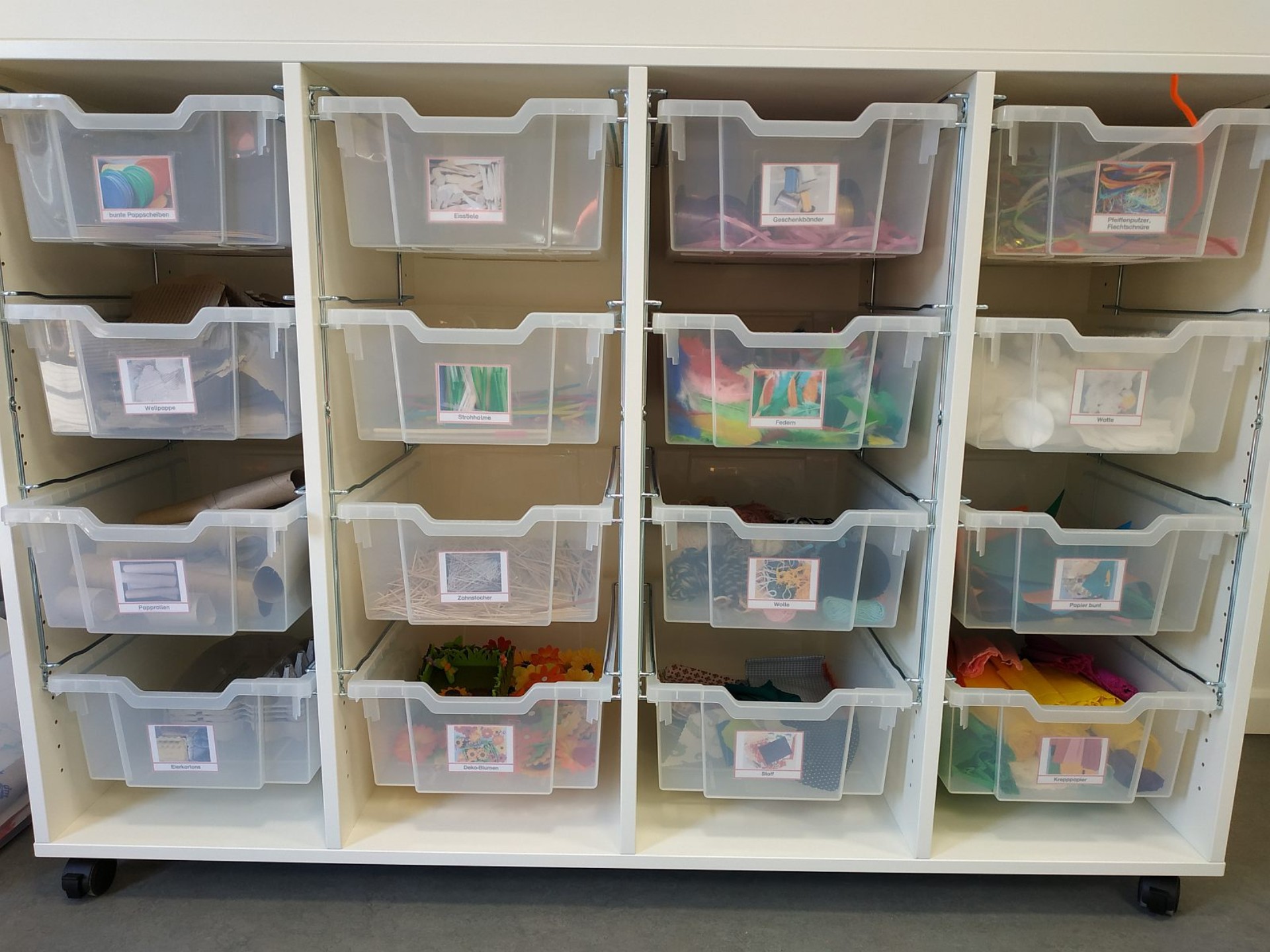 Halbhohes Regal mit transparenten Schubladen, in denen buntes Bastelmaterial gelagert ist.