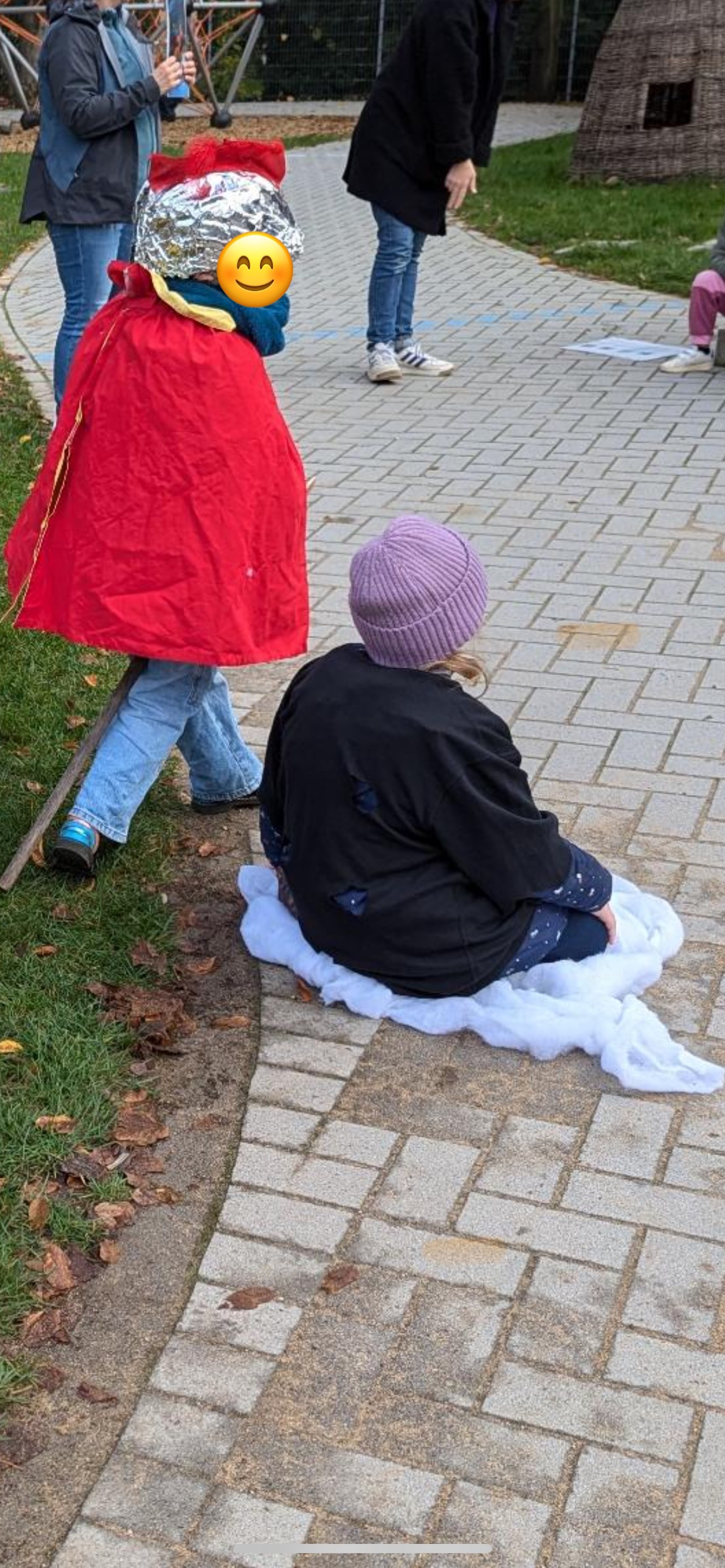 Kinder spielen im freien die St. Martin-Szene nach. Zwei Kinder sind von hinten zu sehen: eines mit Steckenpferd, Helm und rotem Mantel als St- Martin, ein anderes auf dem Boden als Bettler