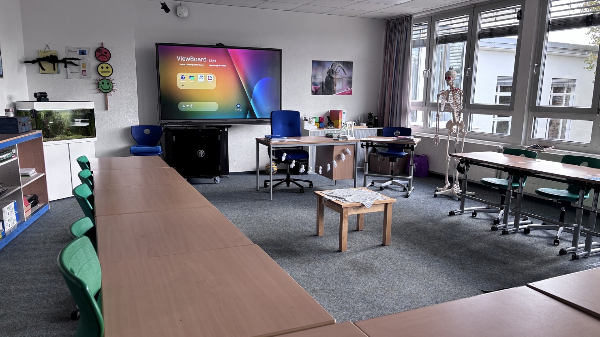 Ein Klassenraum mit Smartboard. Neben dem Pult steht ein Skelett.