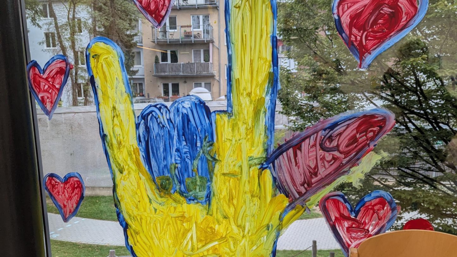 Eine  etwa 1,5 Meter hohe bunte ILY-Hand ist an ein Fenster gemalt. Um die Hand herum sind Herzen gemalt.