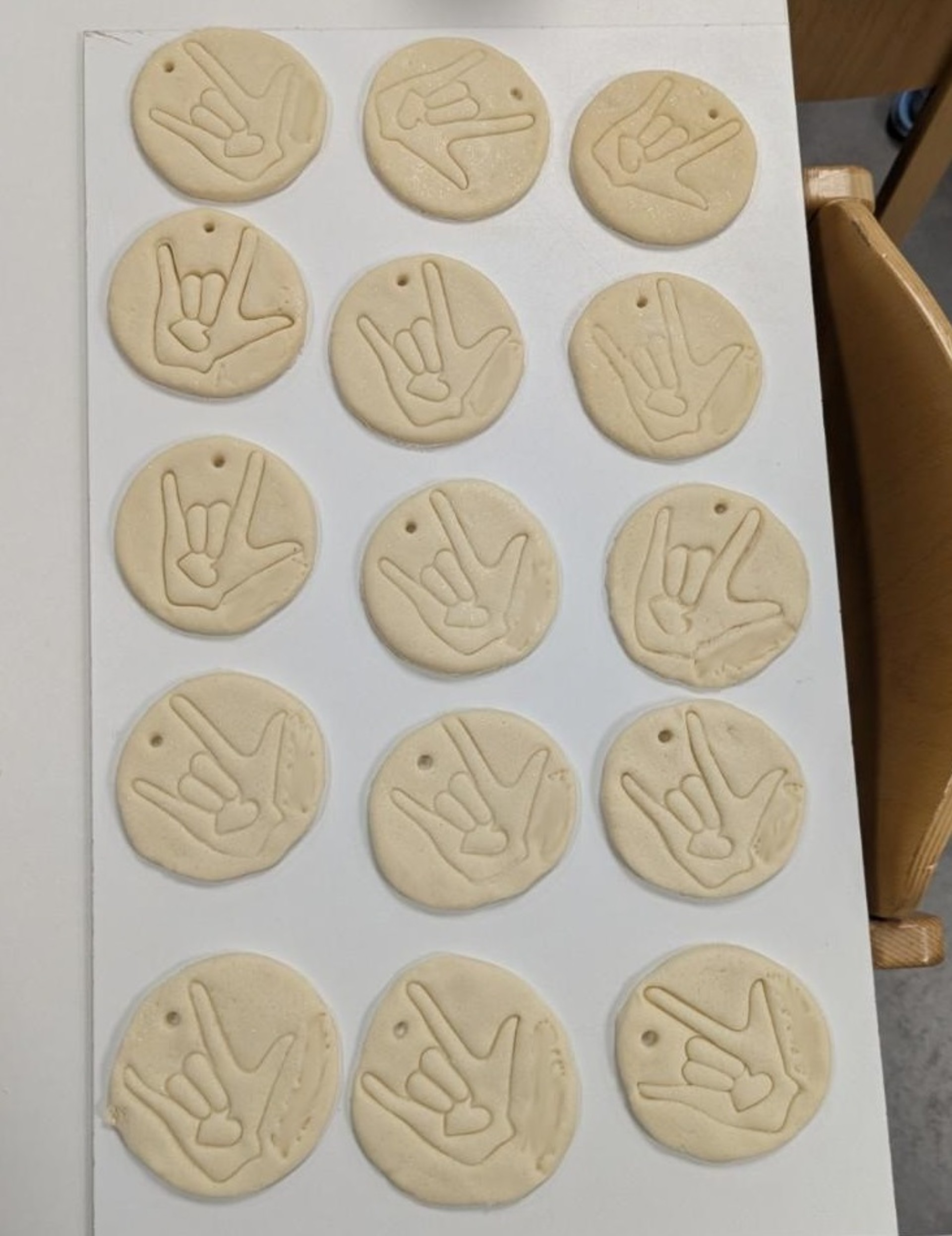 Auf einem Tisch liegen 15  Kreise aus Teig, in die das Motiv der ILY-Hand eingestochen ist.