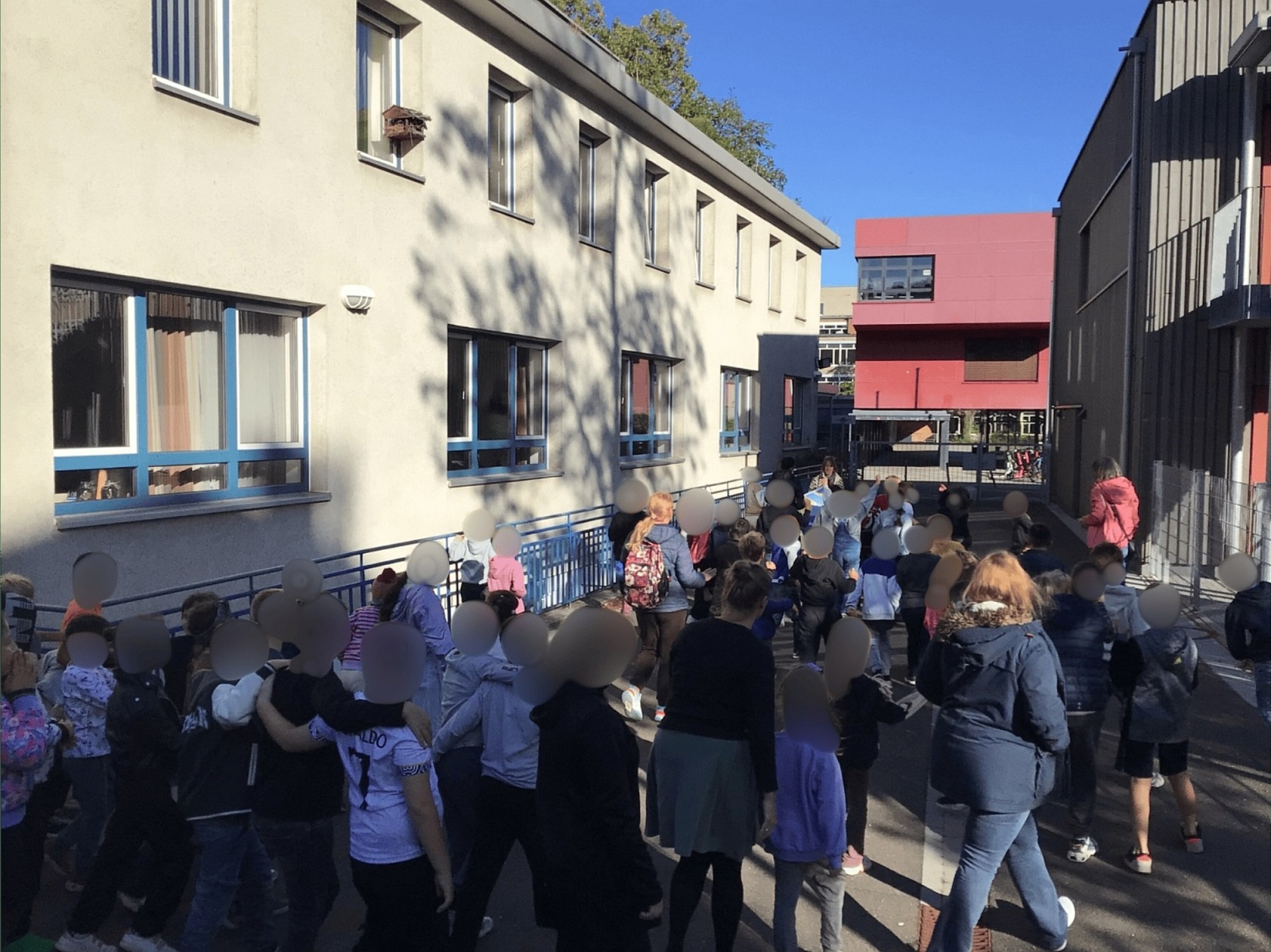 Gruppe von Kindern und Erwachsenen von hinten zwischen zwei Gebäuden.