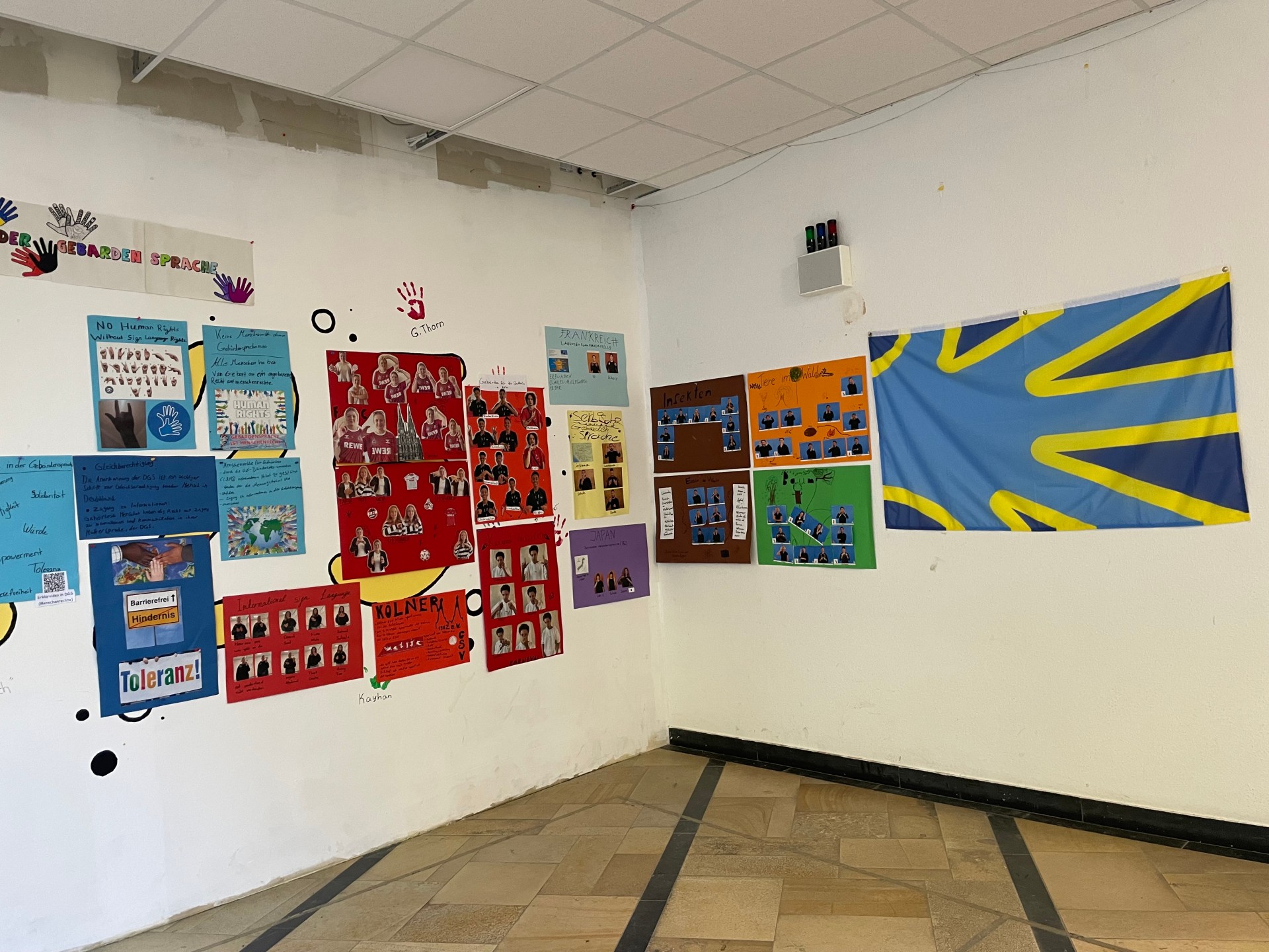 An zwei Wänden hängen Infoplakate , daneben eine große Gehörlosen-Flagge.