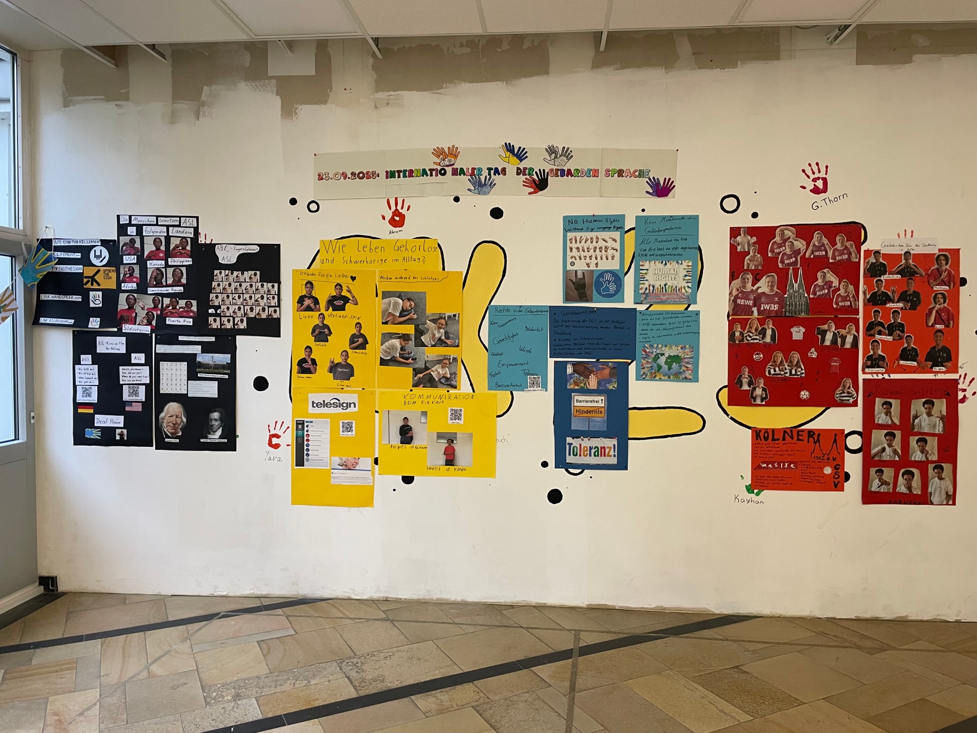 An einer Wand hängen große Infoplakate zu unterschiedlichen Themen rund um die Gebärdensprache.